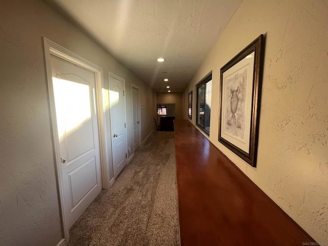 corridor with dark carpet and a textured ceiling