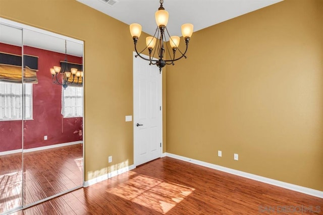 spare room with hardwood / wood-style floors and a chandelier