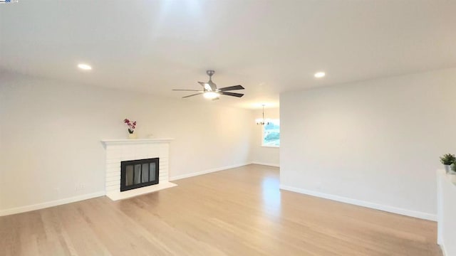 unfurnished living room with light hardwood / wood-style flooring, ceiling fan with notable chandelier, and a fireplace