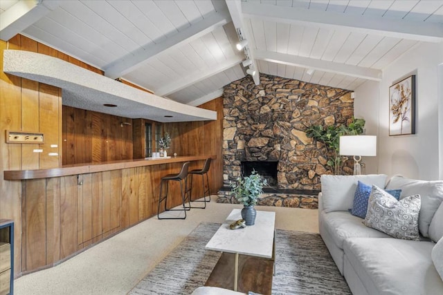 living room with a stone fireplace, wood walls, lofted ceiling with beams, carpet floors, and bar area