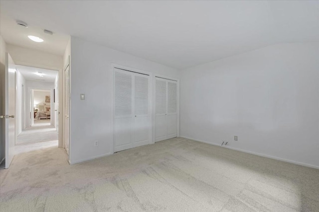 unfurnished bedroom with light carpet and two closets