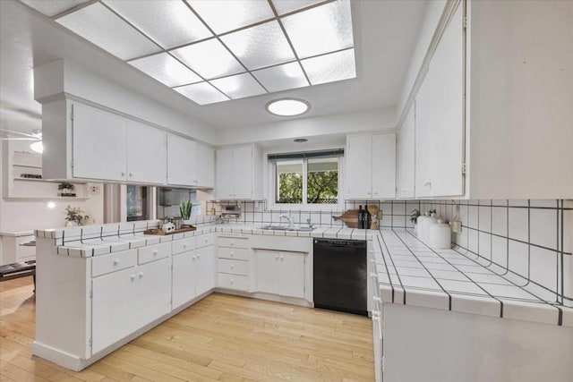 kitchen with white cabinetry, light wood-type flooring, tile counters, dishwasher, and kitchen peninsula