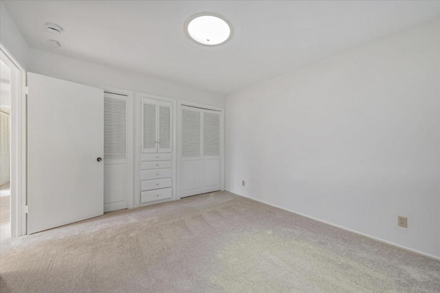 unfurnished bedroom featuring light carpet and two closets