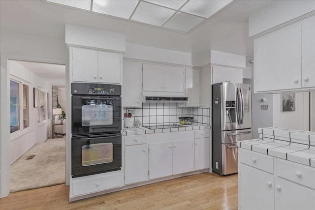 kitchen featuring tasteful backsplash, tile counters, black appliances, and white cabinets