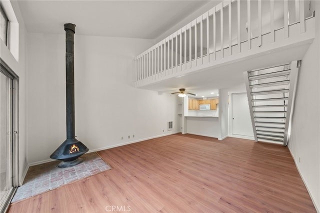 unfurnished living room featuring hardwood / wood-style flooring, a towering ceiling, ceiling fan, and a wood stove