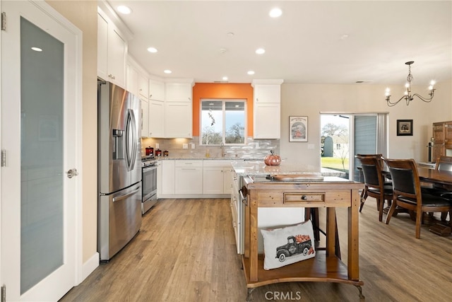 kitchen featuring pendant lighting, appliances with stainless steel finishes, white cabinetry, light hardwood / wood-style floors, and decorative backsplash