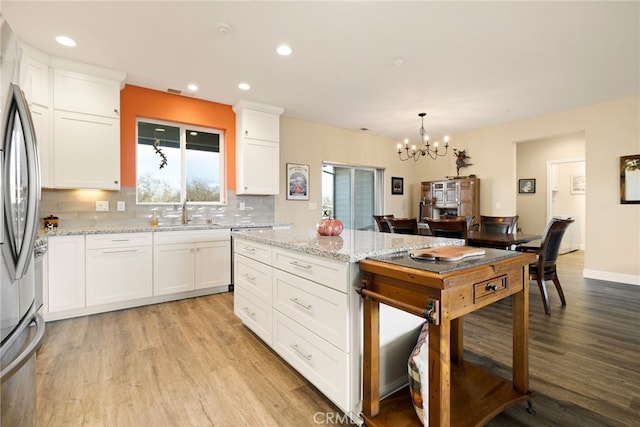 kitchen with stainless steel refrigerator, white cabinetry, backsplash, light stone counters, and light hardwood / wood-style floors