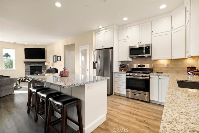 kitchen featuring a kitchen bar, tasteful backsplash, appliances with stainless steel finishes, light stone countertops, and white cabinets