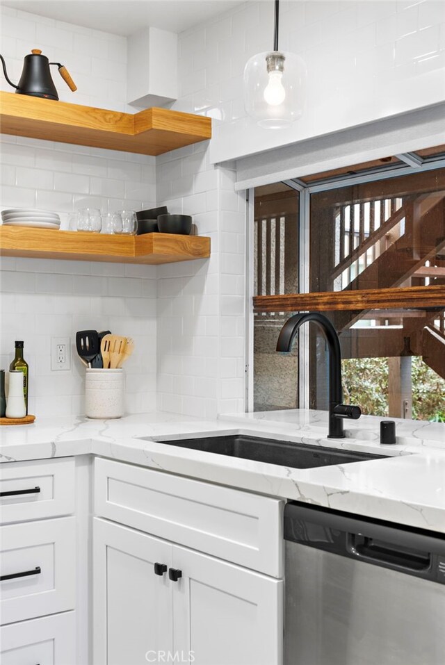 kitchen featuring sink, white cabinetry, light stone counters, decorative light fixtures, and stainless steel dishwasher