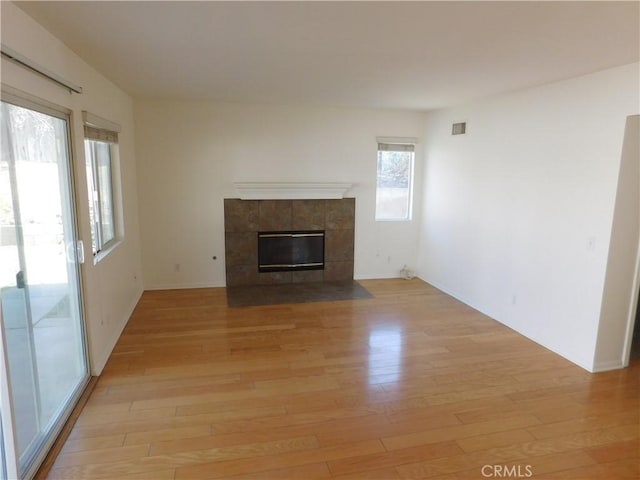 unfurnished living room with a tiled fireplace and light hardwood / wood-style floors