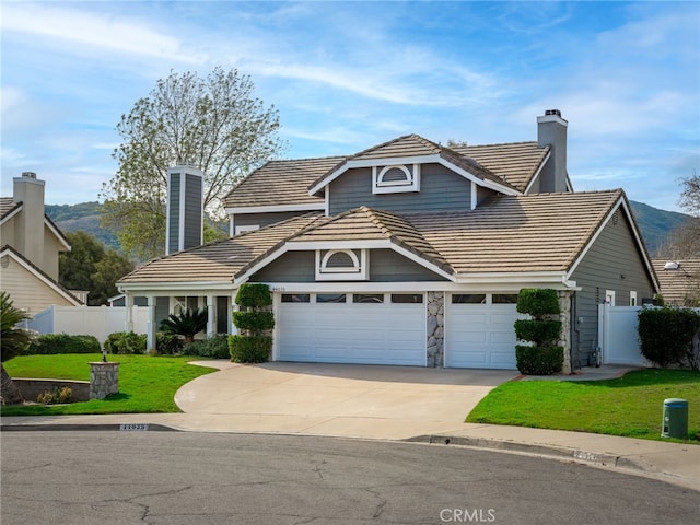 view of front of property with concrete driveway, a tile roof, fence, and a chimney