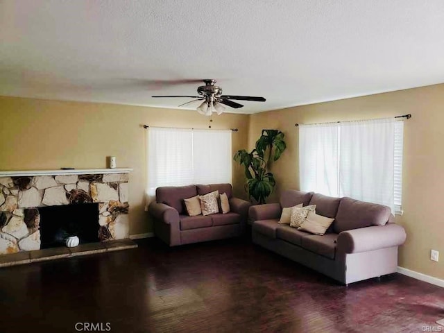 living room featuring a stone fireplace, a wealth of natural light, a textured ceiling, and ceiling fan