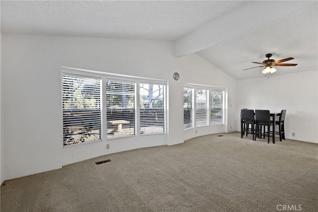 carpeted empty room featuring ceiling fan, lofted ceiling with beams, and a textured ceiling