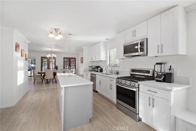 kitchen with sink, a notable chandelier, pendant lighting, stainless steel appliances, and white cabinets