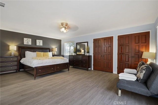 bedroom featuring multiple closets, wood-type flooring, and crown molding