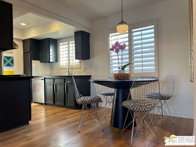 kitchen with light hardwood / wood-style flooring, a breakfast bar area, dishwasher, decorative backsplash, and decorative light fixtures