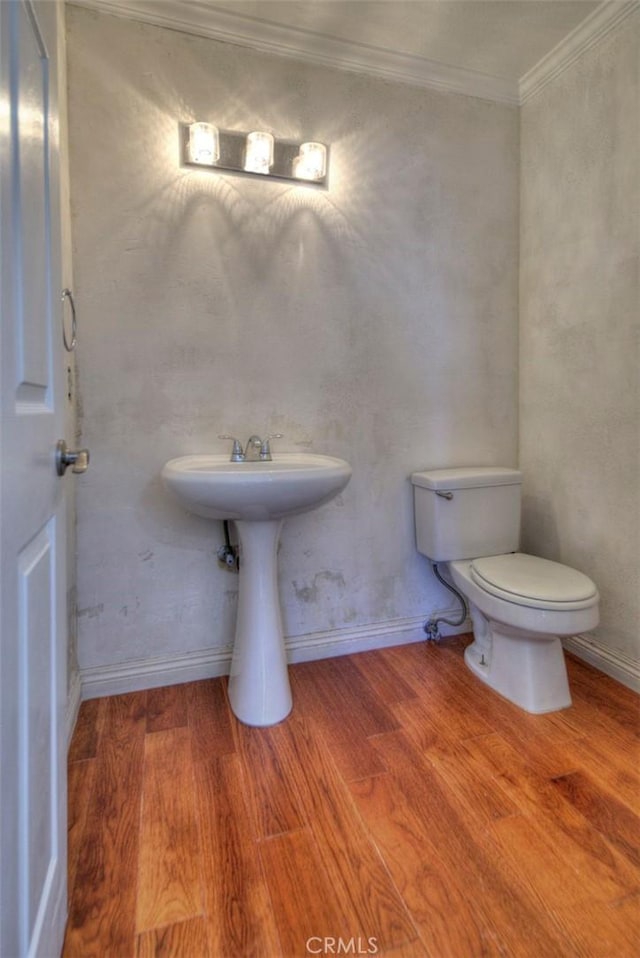 half bath featuring toilet, baseboards, ornamental molding, and wood finished floors