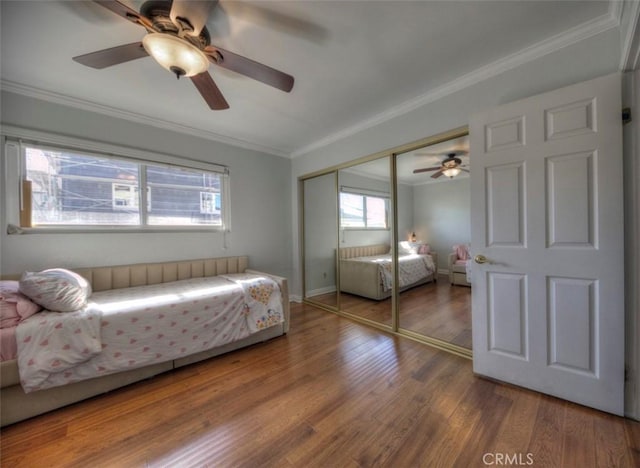 bedroom with ceiling fan, wood finished floors, baseboards, a closet, and crown molding