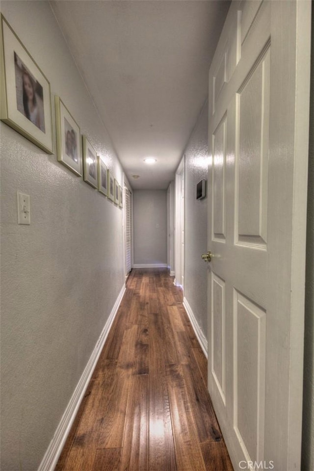 hallway featuring dark wood-type flooring, a textured wall, and baseboards