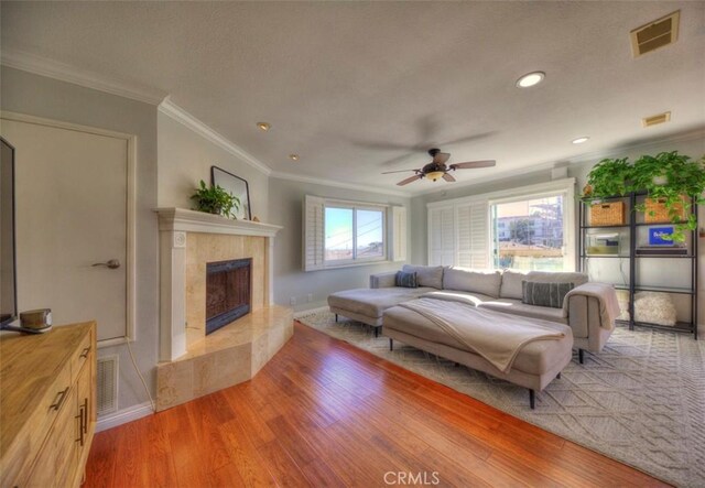 living room featuring crown molding, a fireplace, light hardwood / wood-style floors, and ceiling fan