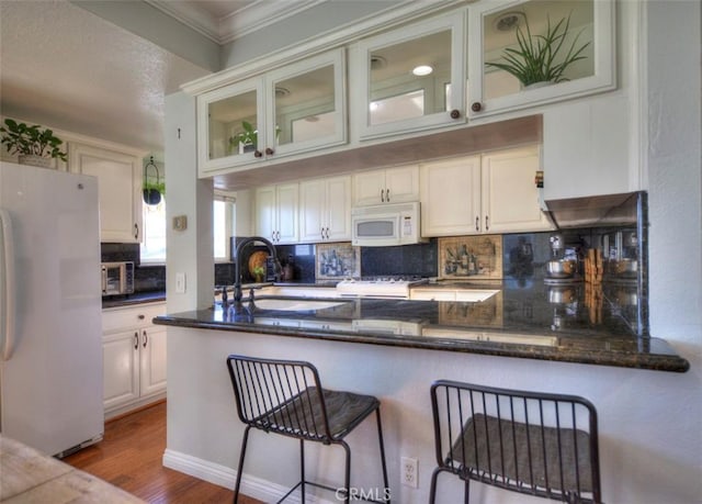 kitchen with white appliances, wood finished floors, a sink, ornamental molding, and decorative backsplash