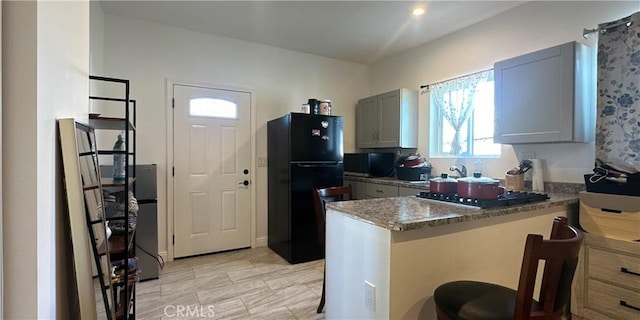 kitchen with gray cabinets, a breakfast bar, dark stone counters, kitchen peninsula, and black fridge