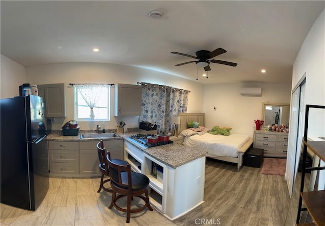 kitchen with sink, gray cabinets, black refrigerator, a wall unit AC, and light stone counters