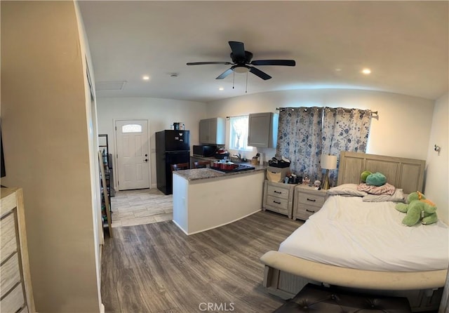 bedroom with wood-type flooring, black refrigerator, sink, and ceiling fan