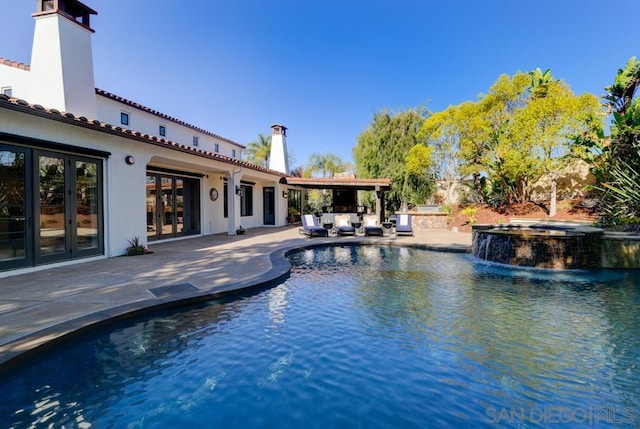 view of swimming pool featuring french doors, a patio area, pool water feature, and an in ground hot tub