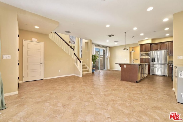 kitchen with a breakfast bar area, an island with sink, pendant lighting, stainless steel appliances, and light stone countertops