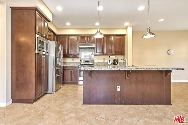 kitchen featuring a kitchen bar, sink, hanging light fixtures, stainless steel appliances, and light stone countertops