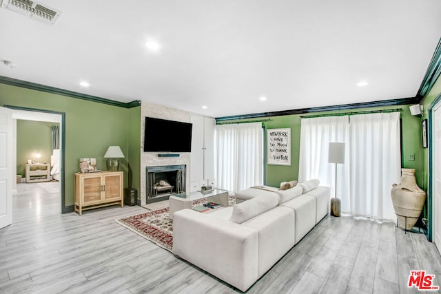 living room featuring a stone fireplace, light hardwood / wood-style flooring, and ornamental molding