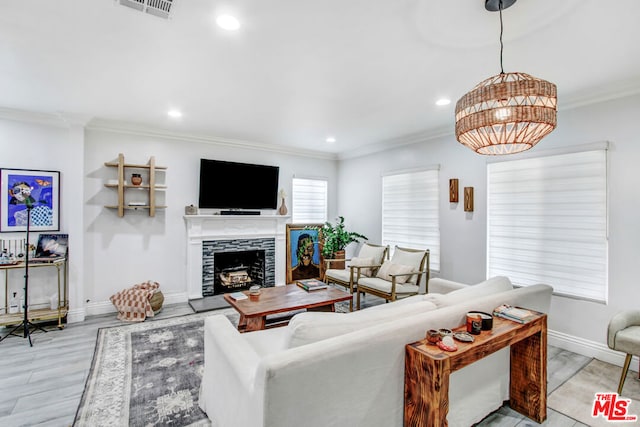 living room with a tiled fireplace, crown molding, and light wood-type flooring