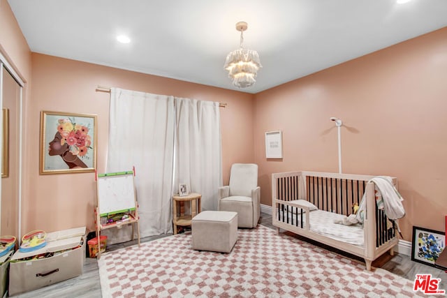 bedroom with a chandelier, light wood-type flooring, a closet, and a crib