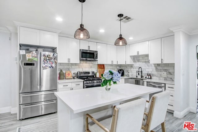 kitchen with tasteful backsplash, white cabinetry, hanging light fixtures, a center island, and stainless steel appliances