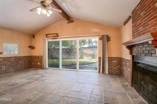 unfurnished living room featuring lofted ceiling with beams, a textured ceiling, ceiling fan, brick wall, and a fireplace