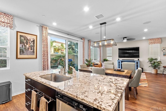 kitchen featuring sink, hanging light fixtures, a center island with sink, dishwasher, and light stone countertops