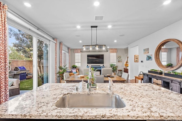 kitchen with light stone counters, sink, decorative light fixtures, and an island with sink