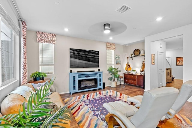 living area with visible vents, a ceiling fan, a glass covered fireplace, light wood-style floors, and recessed lighting