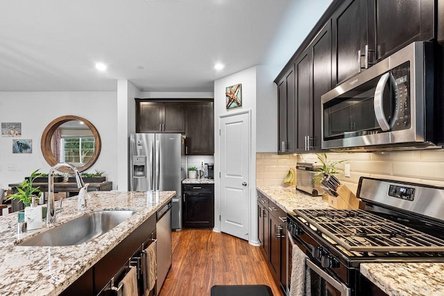 kitchen with dark brown cabinetry, tasteful backsplash, dark wood finished floors, stainless steel appliances, and a sink