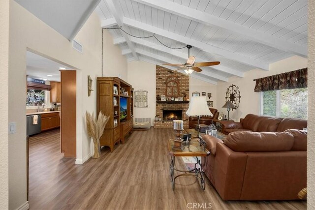 living room with ceiling fan, beam ceiling, high vaulted ceiling, wood-type flooring, and a fireplace