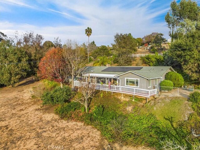 back of property with roof mounted solar panels, fence, and a wooden deck