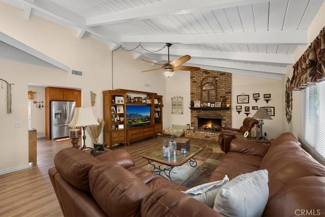 living room featuring ceiling fan, a fireplace, light hardwood / wood-style flooring, and vaulted ceiling with beams