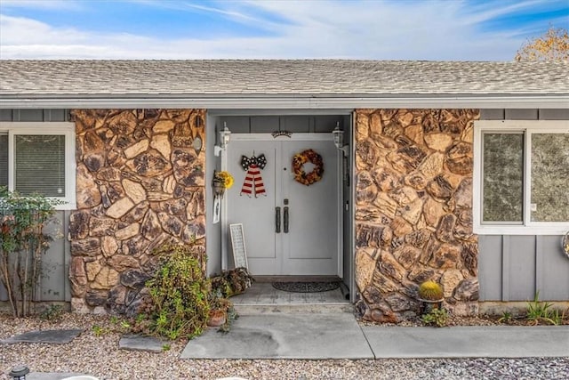 view of exterior entry with board and batten siding, stone siding, and roof with shingles