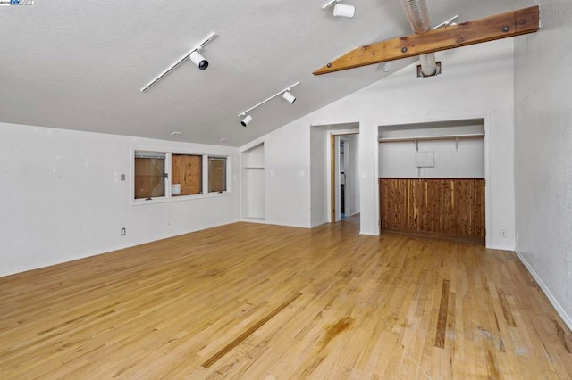 unfurnished living room with rail lighting, lofted ceiling with beams, and light hardwood / wood-style flooring