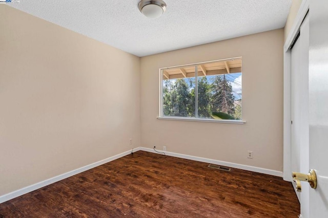 empty room with dark wood-type flooring and a textured ceiling