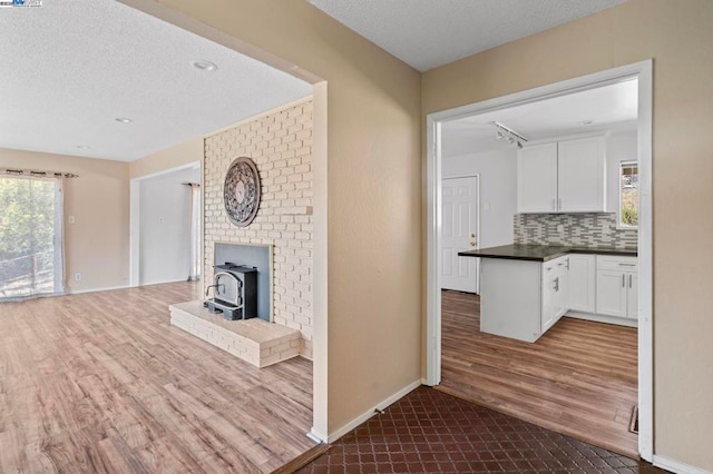 kitchen with hardwood / wood-style flooring, white cabinetry, a textured ceiling, decorative backsplash, and a wood stove