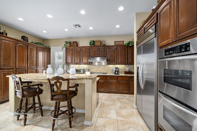 kitchen featuring light stone counters, stainless steel appliances, an island with sink, and a breakfast bar