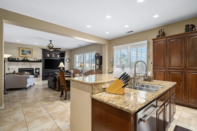 kitchen with light stone counters, a tiled fireplace, sink, and a center island with sink