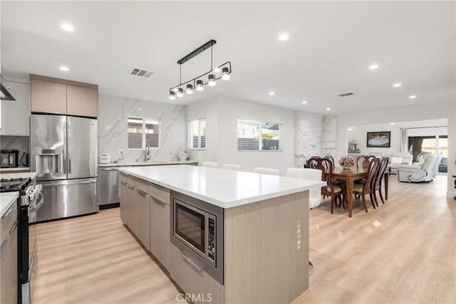 kitchen featuring a kitchen island, pendant lighting, sink, light hardwood / wood-style floors, and stainless steel appliances